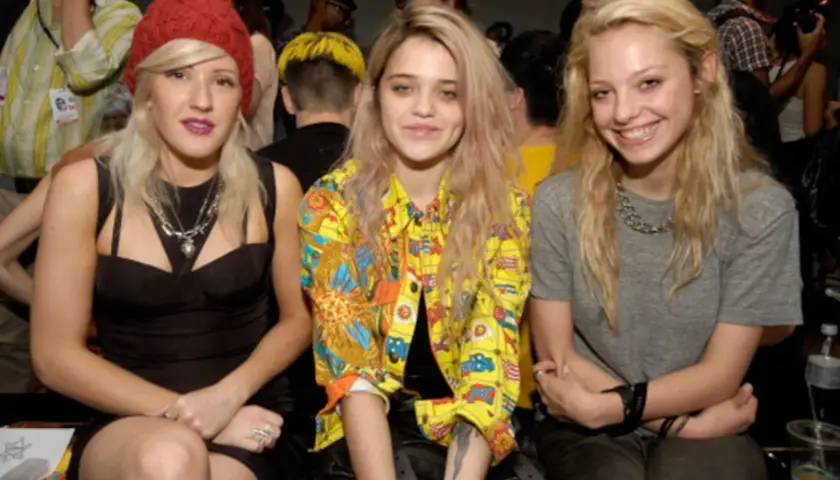 Tres jóvenes con un estilo que evoca el "heroin chic" posan juntas. Una lleva un gorro rojo, otra una chaqueta colorida y la tercera una camiseta gris.
