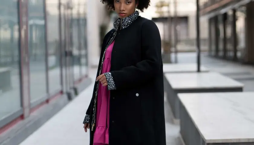 Mujer con estilo urbano y moda oversize, luce un vestido rosa vibrante bajo una chaqueta negra con detalles de lunares.