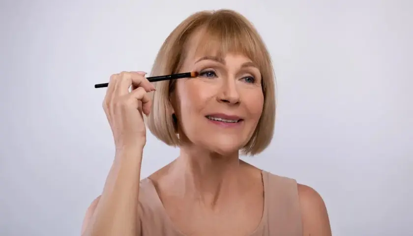 Mujer mayor aplicando sombra de ojos con brocha, aprendiendo como maquillar los ojos a partir de los 50 años para realzar su belleza natural.