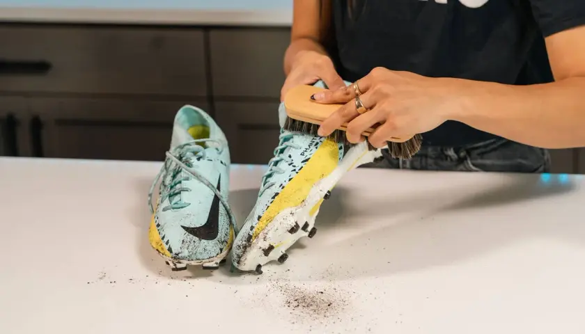 Manos cepillando unas botas de fútbol sucias para aprender como lavar las botas de futbol.