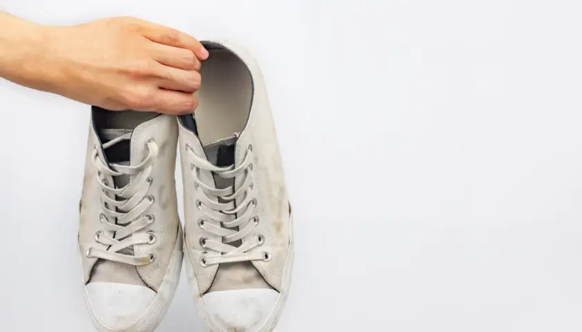Mano sosteniendo un par de zapatillas blancas de tela sucias, listas para limpiar.