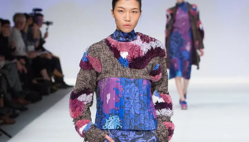 Modelo luce un diseño de upcycling que es una explosión de texturas y colores, con un suéter de tweed y apliques peludos sobre un vestido estampado floral.