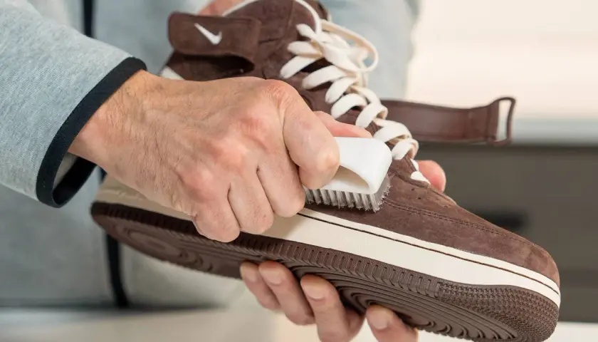 Man limpiando zapatillas de gamuza marrón con un cepillo blanco. Aprende como quitar cera de los zapatos de piel.