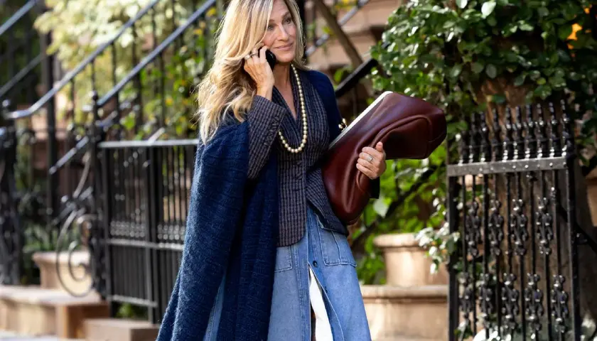 Estilo chic en la ciudad: una mujer con un abrigo azul marino y falda vaquera, combinando granate y verde con su bolso y el follaje.