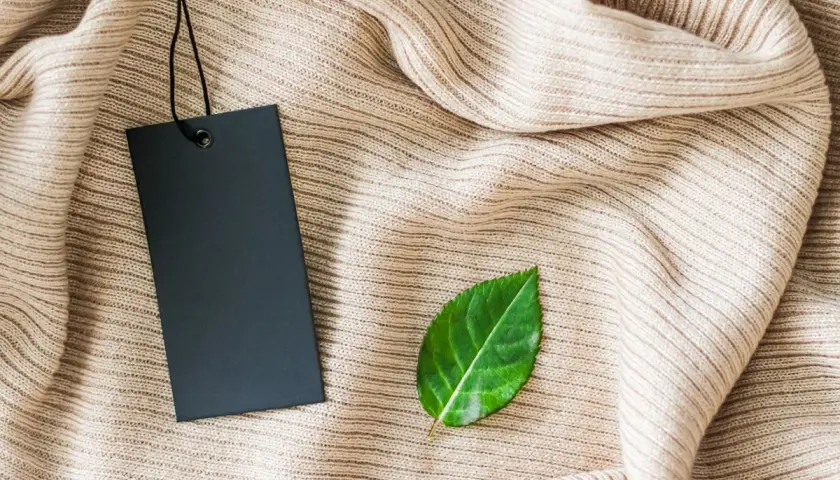 Etiqueta negra sobre tejido beige, con una hoja verde al lado. Símbolo de una marca sostenible.