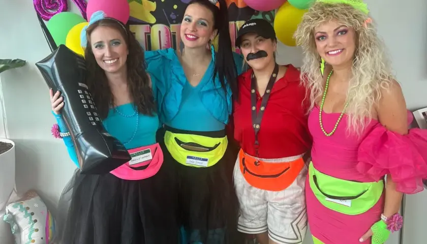 Cuatro amigas celebran una fiesta moda de los 80 con atuendos coloridos, riñoneras y peinados voluminosos.
