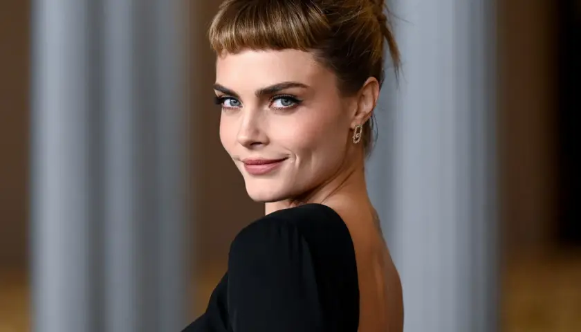 Cara Delevingne, con su mirada penetrante y un peinado recogido con flequillo, luce un elegante vestido negro de espalda descubierta.