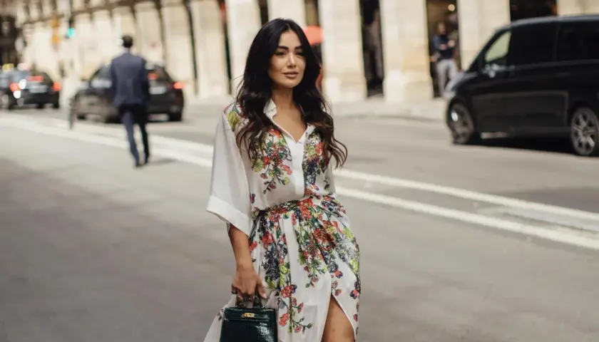 Mujer con vestido estampado floral, estilo manga francesa, pasea por París con un bolso verde.