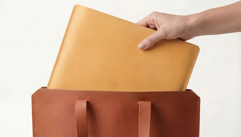 Mano colocando un portátil de piel vegetal en un bolso de cuero.