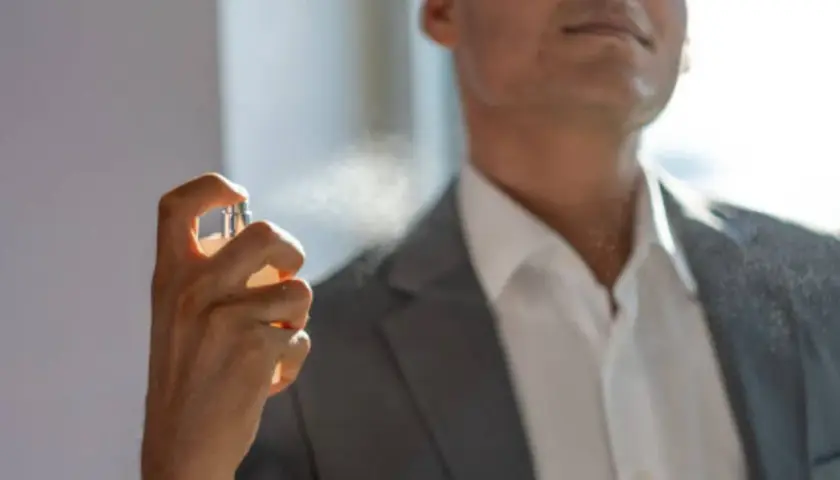 Hombre aplicándose perfume con un frasco rociador.