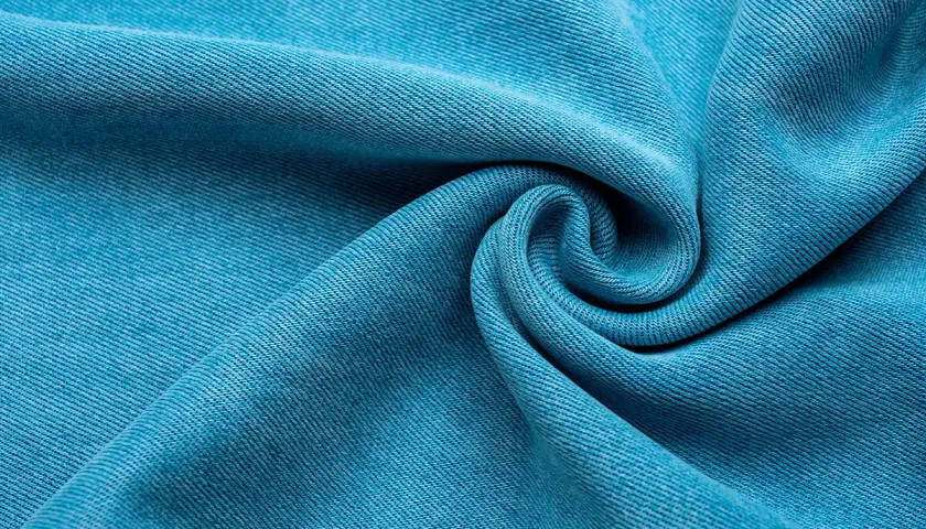 Textura de tela Tencel azul vibrante, suave y con caída, que evoca la comodidad y sostenibilidad de este tejido.