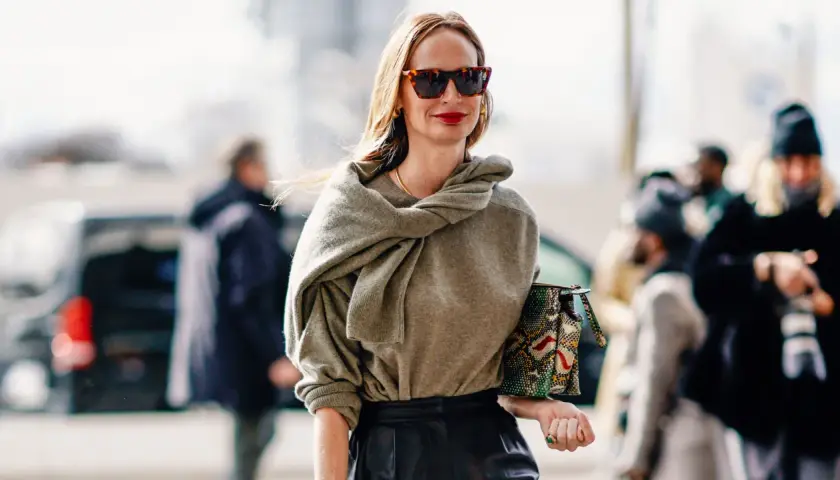 Mujer de unos 40 años con un look casual chic, gafas de sol, suéter gris y bolso estampado.