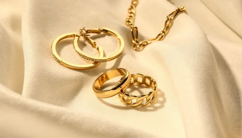 Anillos y cadena dorados sobre tela. Los aros tienen pequeñas piedras preciosas incrustadas, como si fueran diamantes.