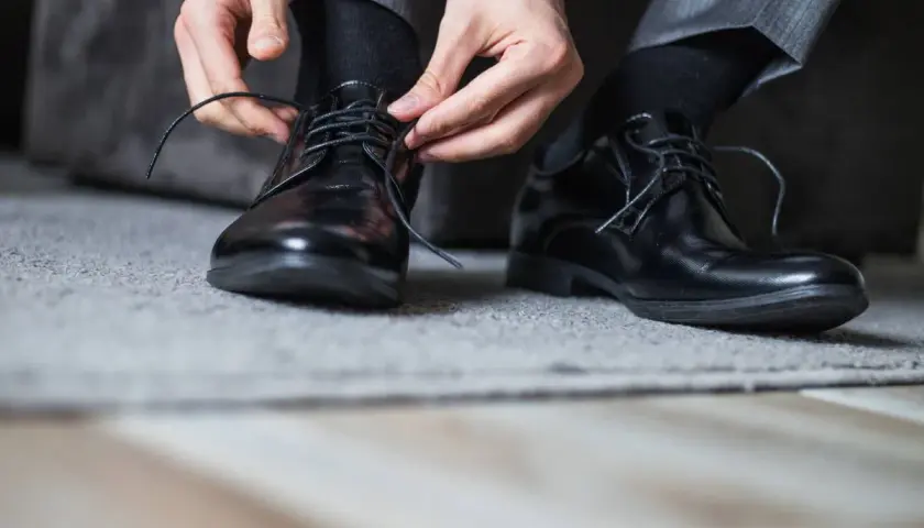 Man se ata los cordones de sus zapatos de piel negros, preparándose para evitar rozaduras.
