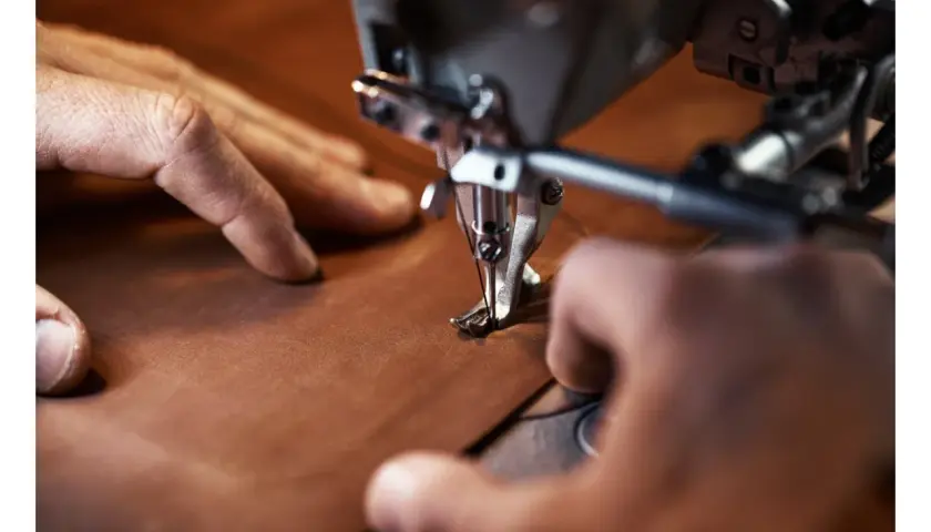 Manos cosiendo con precisión una pieza de cuero vegetal en una máquina de coser industrial.