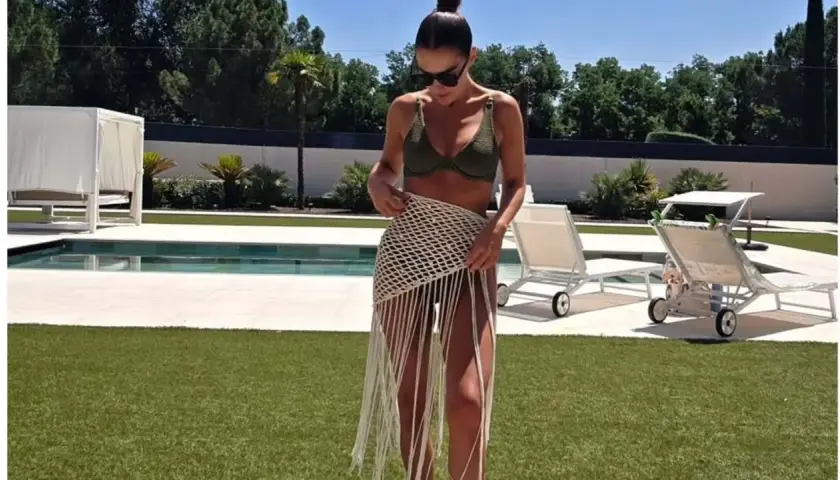 Paula Echevarría luce un bikini verde y una falda de crochet con flecos junto a la piscina, disfrutando del sol.
