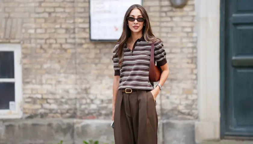 Mujer con estilo, combinando un pantalón marrón de tiro alto con una blusa a rayas marrones y blancas.