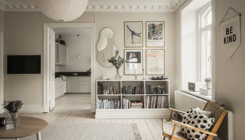 Salón con estilo de Estocolmo: estanterías blancas llenas de libros, arte en las paredes, silla de madera y alfombra gris.