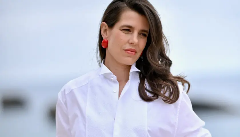 Carlota de Monaco, con pendientes rojos y camisa blanca, mira a lo lejos.