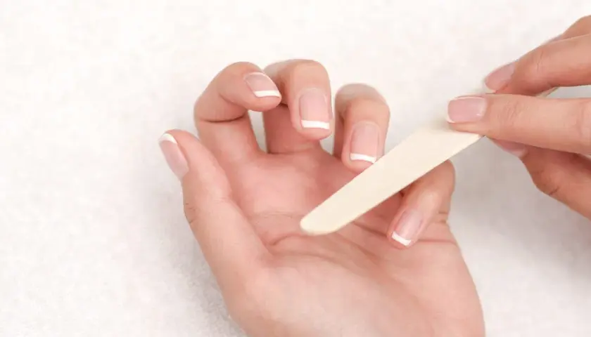 Manos limándose las uñas francesas. Una guía visual para saber como quitar uñas de gel.