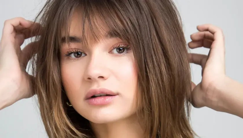 Chica con flequillo desfilado y cabello castaño, ideal para cortes de pelo para cara redonda.
