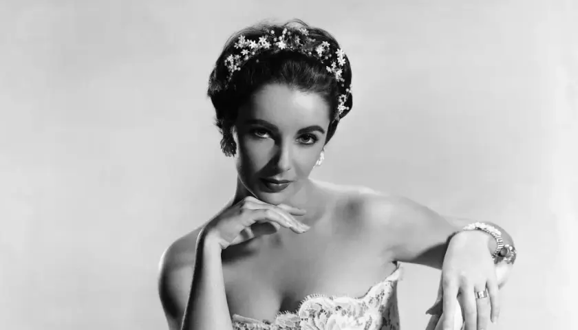 Elizabeth Taylor, con un tocado floral y un vestido de encaje, posa con elegancia.