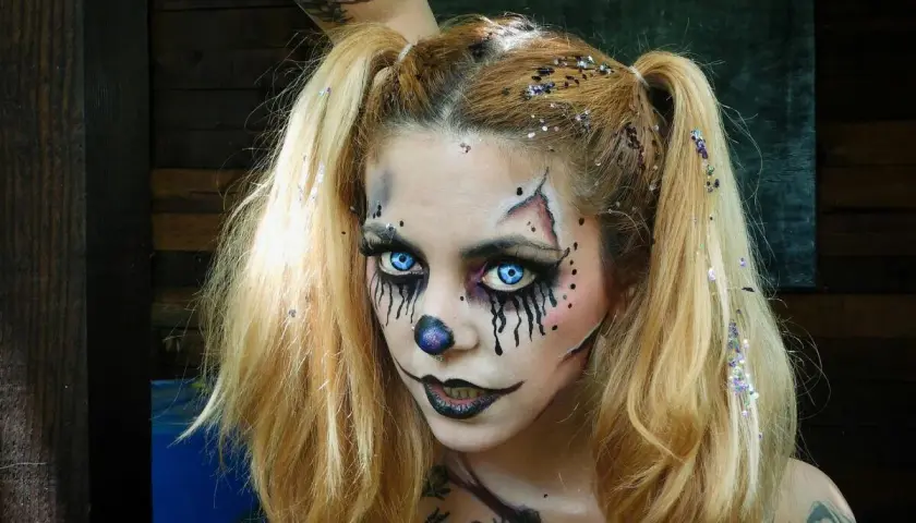 Chica con maquillaje de halloween de payaso aterrador, ojos azules brillantes, nariz de payaso y purpurina en el cabello.