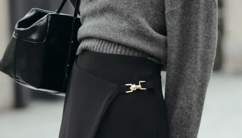Chaqueta gris y bolso negro sobre falda negra larga con detalle dorado. Un look elegante para saber como combinar una falda negra larga.