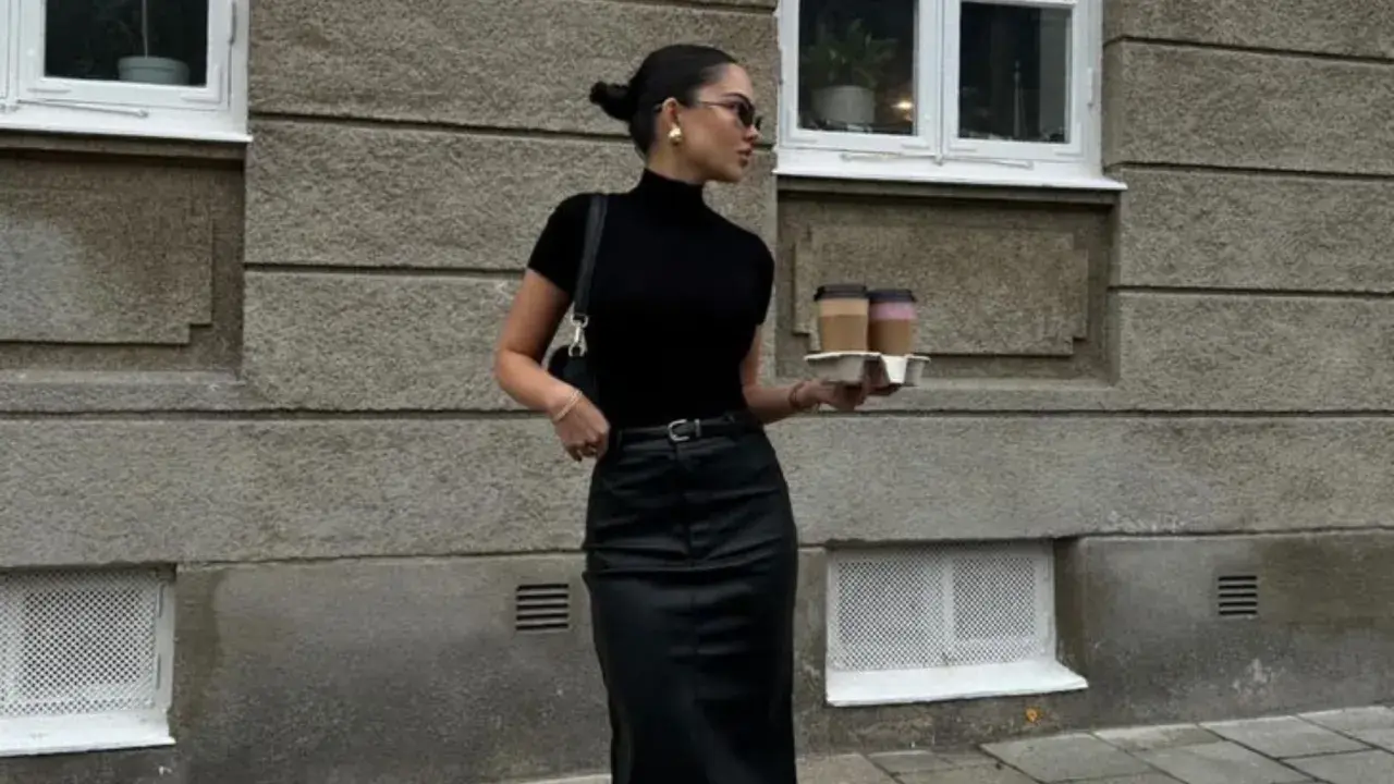 Chica goth con estilo, lleva un top negro de cuello alto, falda de cuero y dos cafés.