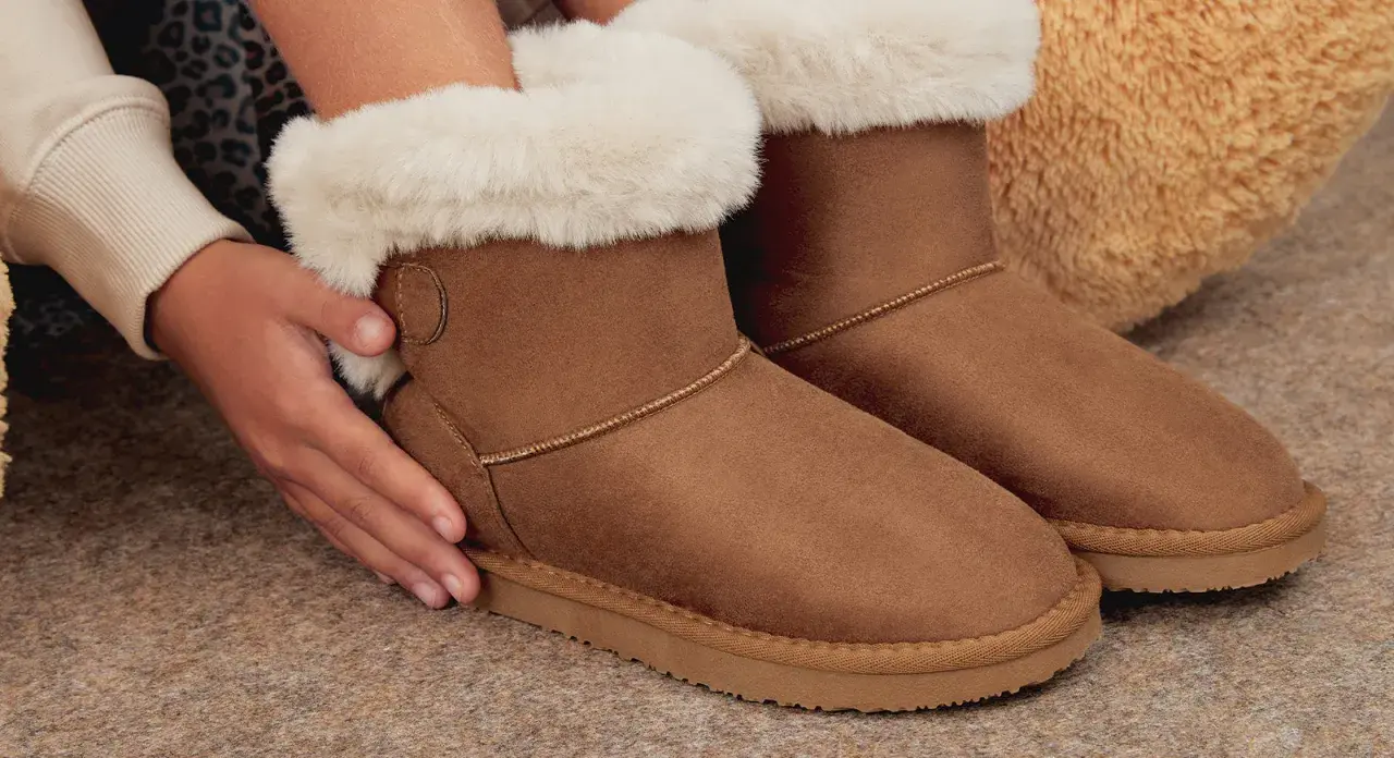 Manos cuidando unas botas de pelo marrones, perfectas para aprender como limpiar botas de pelo y mantenerlas como nuevas.