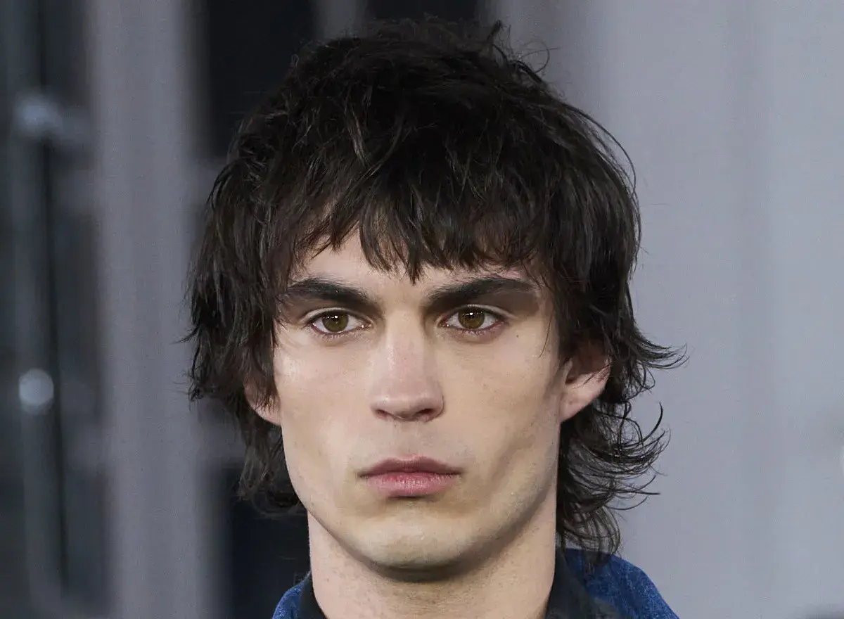 Joven con un moderno corte mullet, cabello oscuro y despeinado, mirada intensa y cejas marcadas.