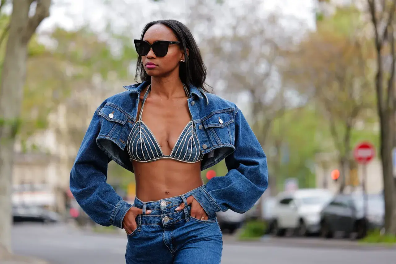 Mujer con gafas de sol luce un conjunto de **denim on denim**: chaqueta corta y sujetador de pedrería, combinados con jeans.