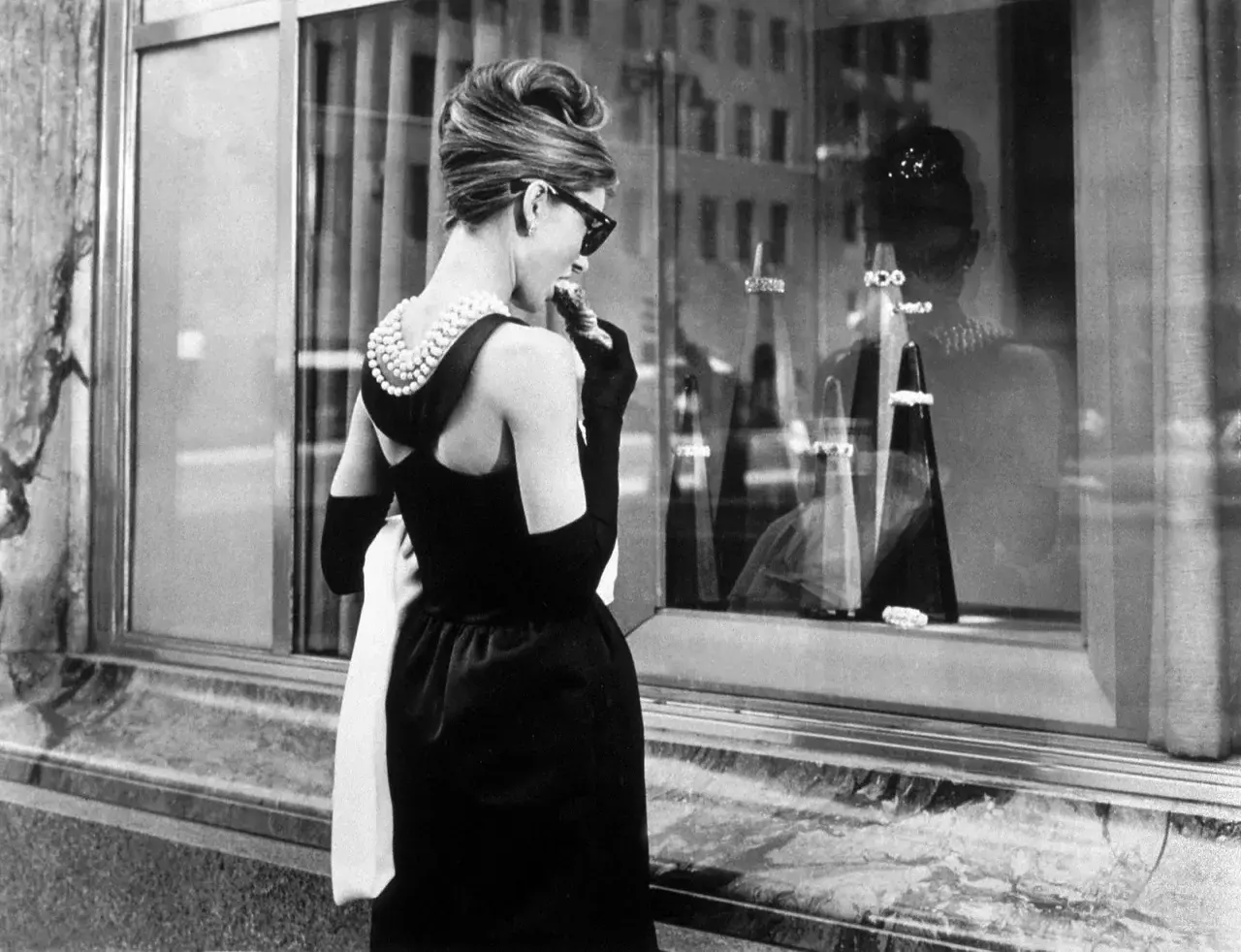 Audrey Hepburn, icónica en su vestido negro y perlas, disfruta de un pastel frente a Tiffany's.