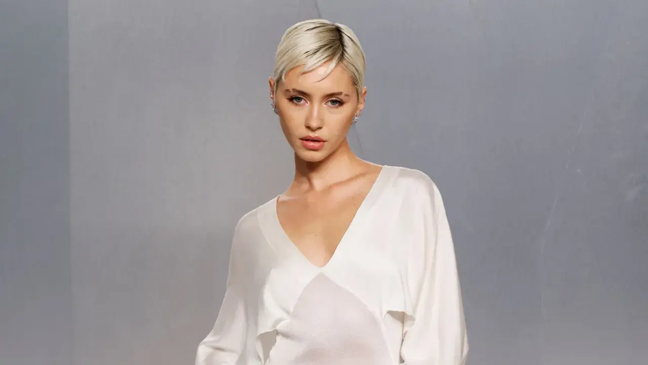 Iris Law, con su corte de pelo rubio platino y un top blanco de seda, posa con una mirada intensa.