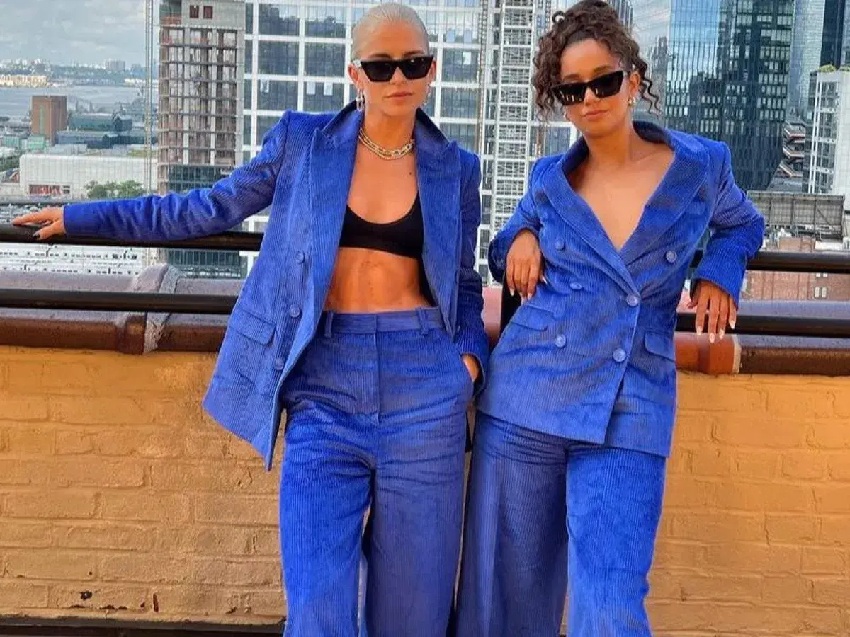 Dos mujeres posan con trajes de pana azul eléctrico, con la ciudad de fondo.