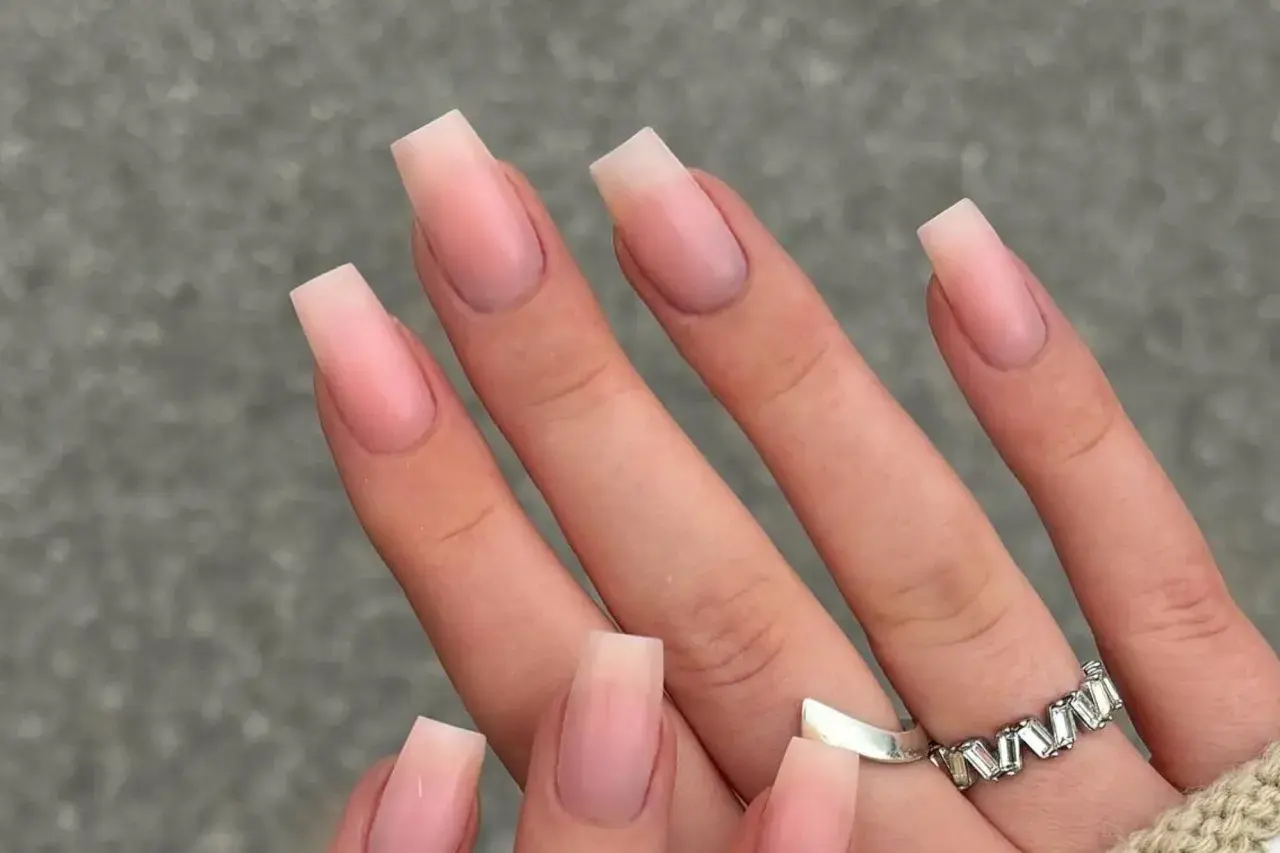 Manos con uñas naturales bonitas en forma cuadrada, con un degradado sutil de rosa pálido a transparente.