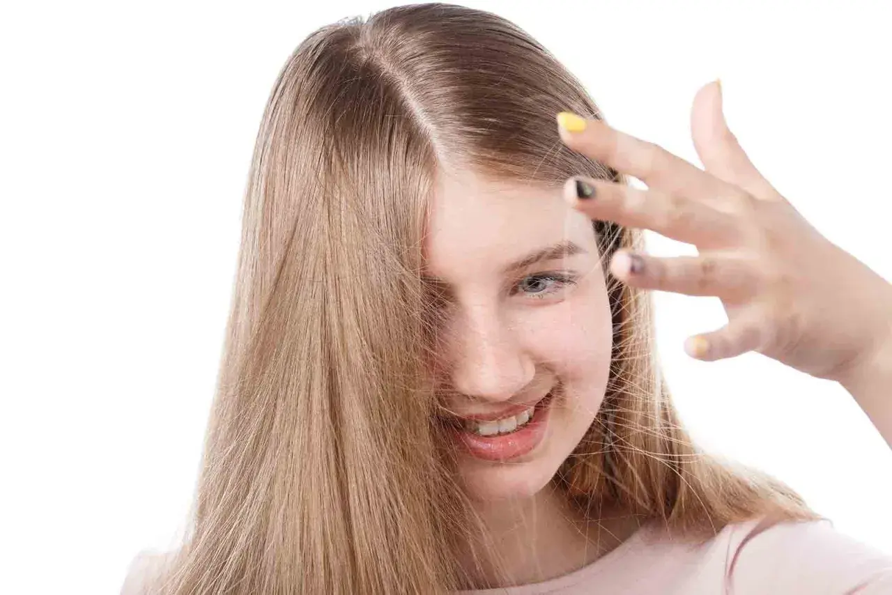 Chica sonriente con cabello rubio que se electrifica. Descubre cómo quitar la electricidad del pelo para un look suave.