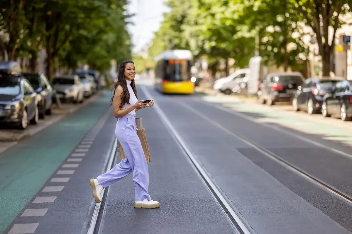 Mujer sonriente cruza la calle con bolsas, disfrutando de su estilo de slow fashion.