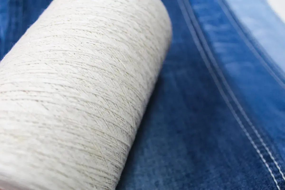 Rollo de hilo crudo sobre tela vaquera azul. El hilo es la base del denim, un tejido con un rico significado cultural.