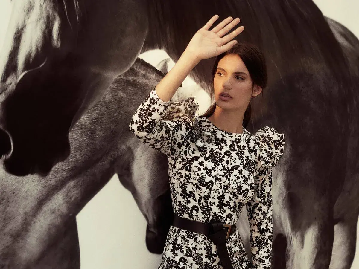 Inés Domecq, con su vestido floral, se protege del sol junto a la imponente silueta de un caballo.