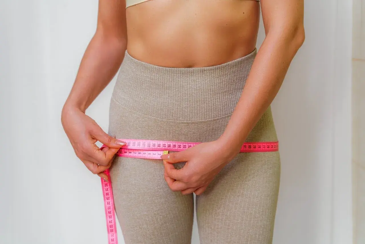 Mujer midiendo su cintura con cinta métrica rosa, enfocándose en la zona de los **hip dips**.