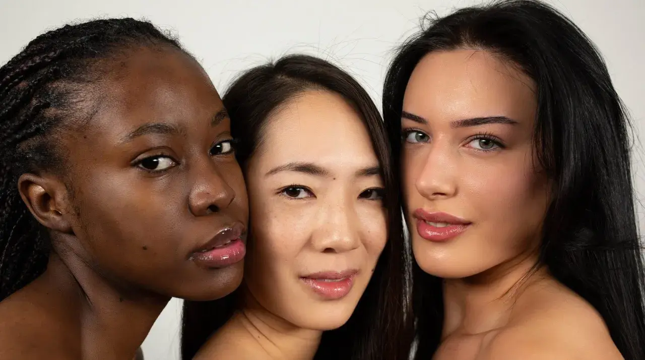 Tres mujeres de diferentes etnias, una con piel **color negro**, se miran a la cámara con labios brillantes.