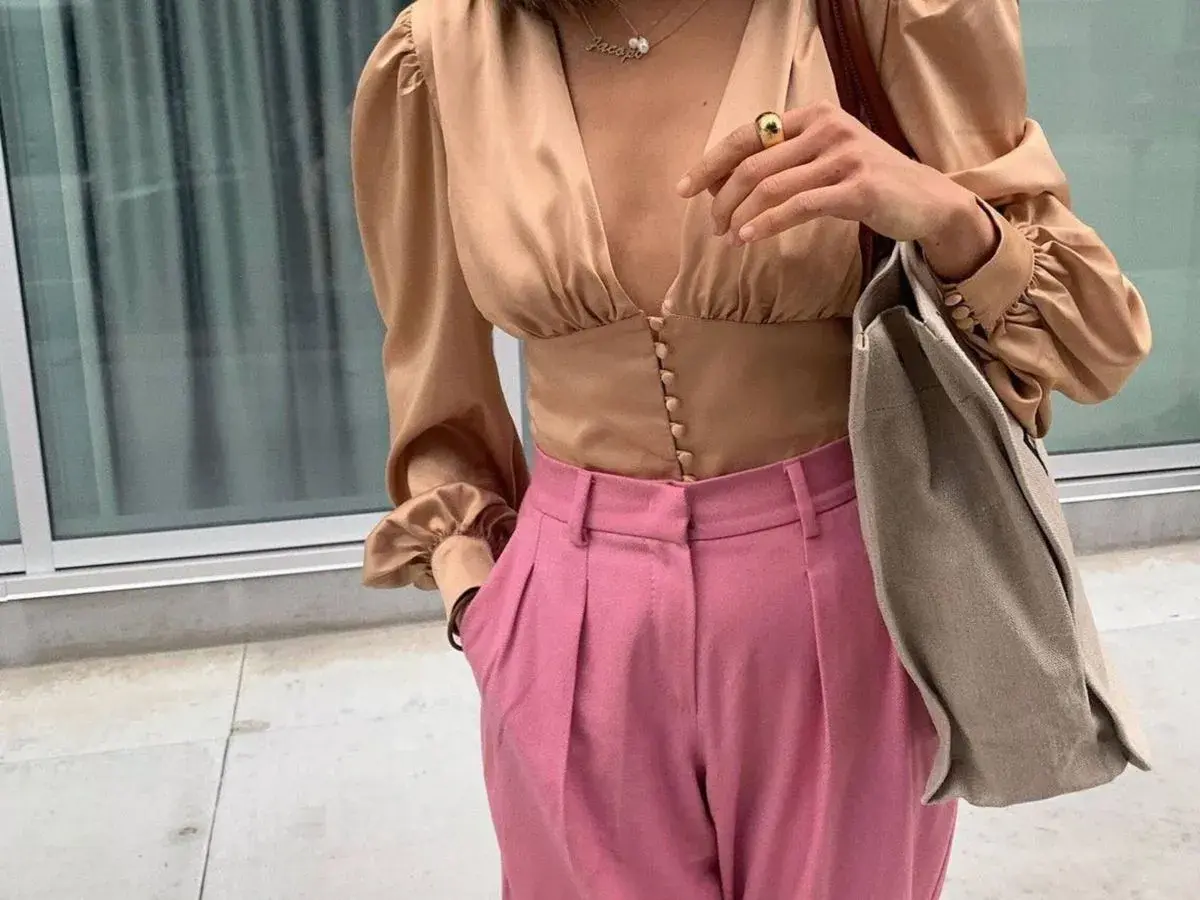 Elegante blusa beige satinada con pantalones rosa vibrante. Un look chic que demuestra los colores que combinan con el beige.