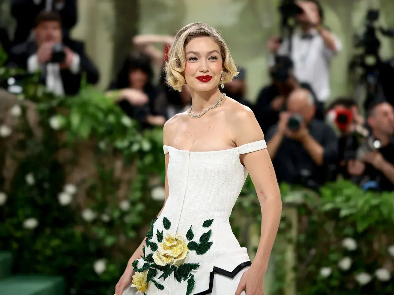 Gigi Hadid deslumbrante en la Met Gala, con un vestido blanco adornado con rosas amarillas y verdes.