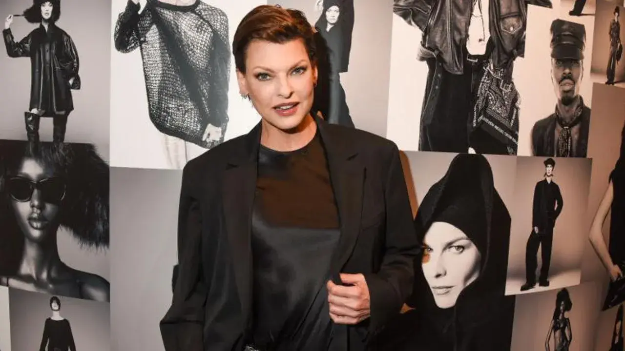 Linda Evangelista hoy, posando con confianza frente a un collage de sus icónicas fotos de moda.