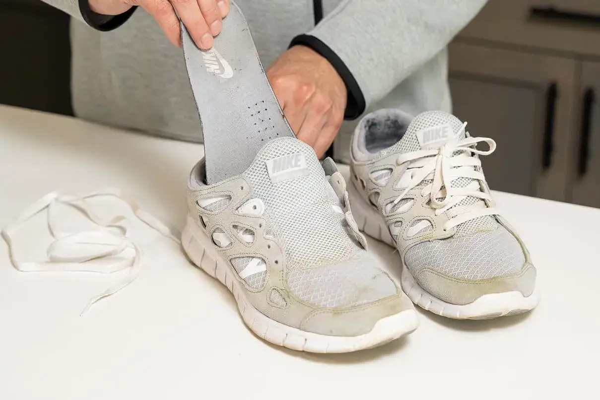 Man removes insole from dirty white Nike sneakers. Learn como quitar desteñido en zapatillas blancas.