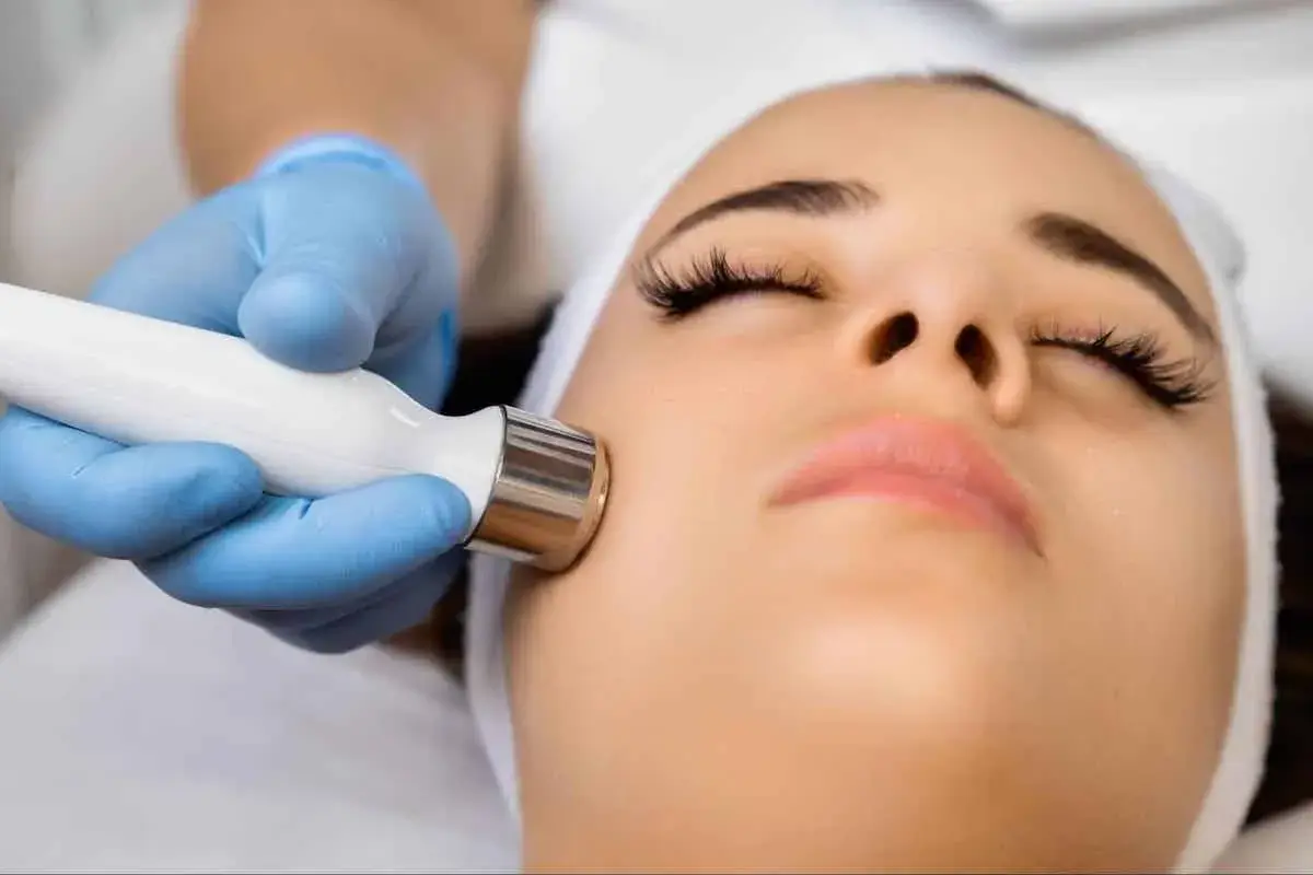 Un rostro recibe un tratamiento facial con exosomas, aplicado con un dispositivo de mano por un profesional con guantes azules.
