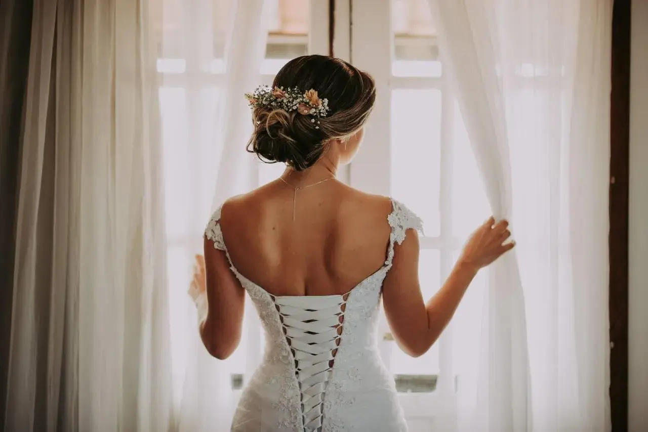 Novia con un juvenil recogido de boda adornado con flores, luciendo su espalda con un corsé de encaje.