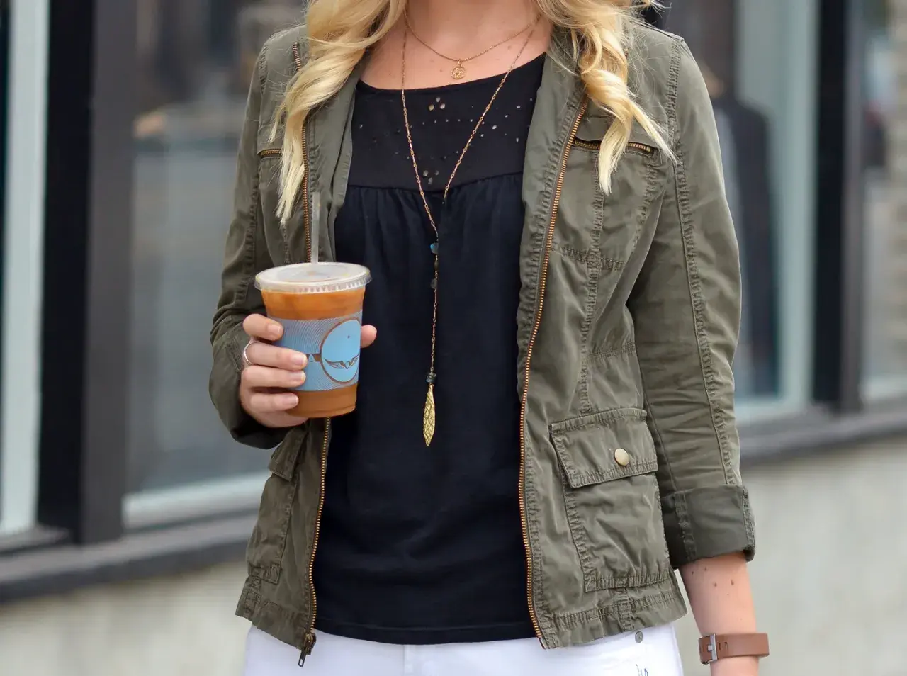 Chica con chaqueta verde militar y café helado.