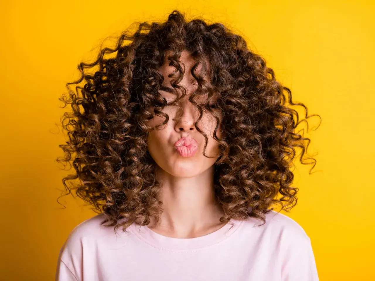 Mujer con pelo corto rizado y labios en forma de beso, sobre fondo amarillo.